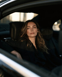 Woman with long hair sits in a car seat, gazing out the window with a calm expression.